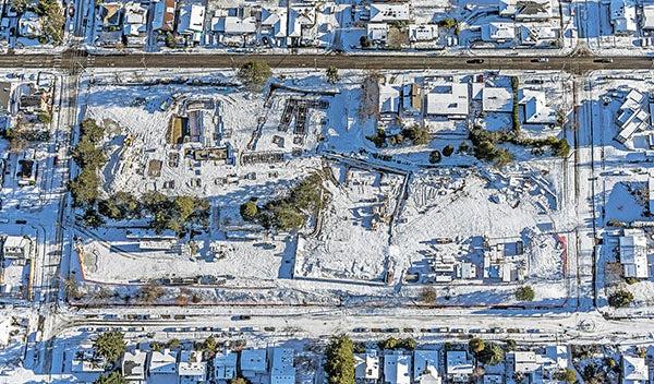 an aerial view of a construction site covered in snow with a cleared street above it and snowy streets around it