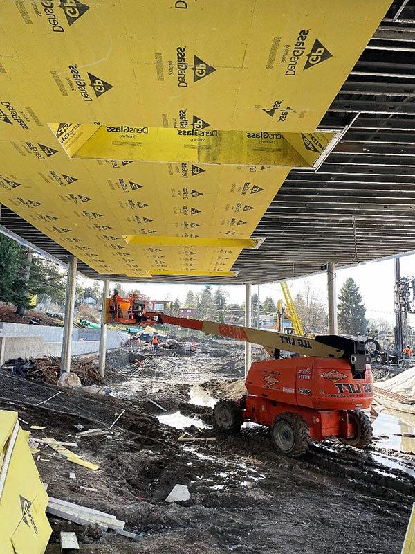 a muddy outdoor area has a partially completed roof with yellow material being installed