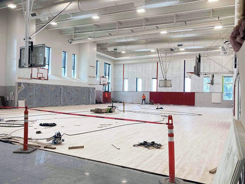 a large two-story room has backetball hoops and a wood floor is being installed